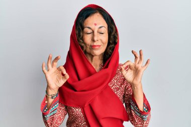 Orta yaşlı İspanyol kadın geleneksel Sherwani sari giysisi giyer rahatlar ve gözleri kapalı gülümser parmaklarıyla meditasyon hareketi yapar. yoga konsepti. 