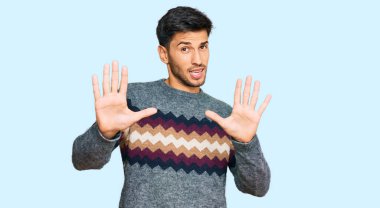 Kış süveteri giyen genç yakışıklı adam korku ifadesi yüzünden korkmuş ve dehşete düşmüş. El hareketlerini durdur, şok içinde bağır. panik konsepti. 