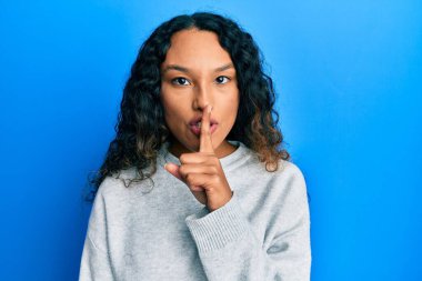 Gündelik giysiler giyen genç Latin kadın parmakları dudaklarında sessiz olmak istiyor. sessizlik ve gizli konsept. 