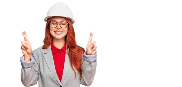 年轻的红头发女人戴着建筑师的硬礼帽 戴着手势 微笑着 闭上了眼睛 幸运与迷信的概念 — 图库照片