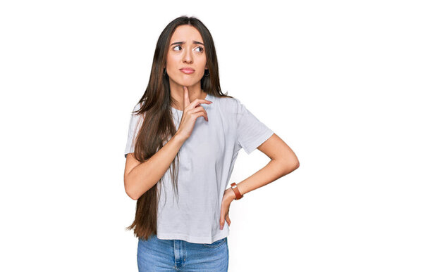 Young hispanic girl wearing casual white t shirt thinking concentrated about doubt with finger on chin and looking up wondering 