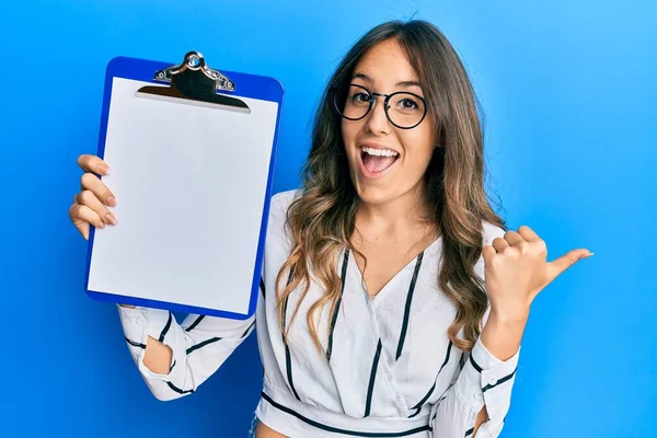 Jovem Morena Segurando Prancheta Com Espaço Branco Apontando Polegar Para — Fotografia de Stock