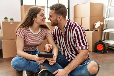 Yeni evimizde akıllı telefon kullanarak mutlu bir şekilde gülümseyen beyaz bir çift..