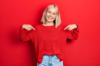 Güzel sarışın kadın, günlük kırmızı süveter giyiyor. Kendine güvenen, gülümseyen, kendini gururlu ve mutlu gösteren.. 