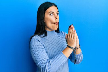 Güzel esmer kadın elinde Katolik tespihi tutarak dua ediyor. Ağzı balık yüzü yapıyor ve şaşı bakıyor. Deli ve komik.. 