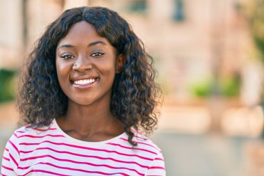 Genç Afrikalı Amerikalı kız gülümseyerek şehirde mutlu mesut duruyor..