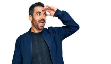 Gündelik kıyafetler giyen genç İspanyol adam çok mutlu ve gülümsüyor. Elleri başının üzerinde uzaklara bakıyor. arama kavramı. 