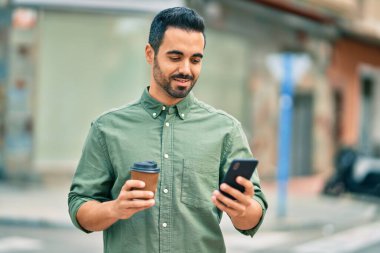 Genç İspanyol adam şehirde akıllı telefon kullanarak mutlu gülümsüyor..