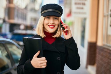 Genç sarışın kadın gülümsüyor. Şehirdeki akıllı telefondan konuşuyor..
