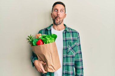 Sakallı yakışıklı bir adam elinde poşetle market alışverişi yapıyor dudaklarıyla balık suratı yapıyor, çılgınca ve komik bir jest. Komik ifade. 