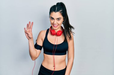 Spor kıyafetleri giyen ve kulaklık takan İspanyol genç kız dört numarayı gösterip işaret ederken kendinden emin ve mutlu gülümsüyor.. 