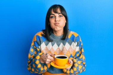 Bir fincan kahve içen genç İspanyol kadın komik yüzlü yanakları şişiriyor. Ağzı havayla şişer, havayı yakalar.. 