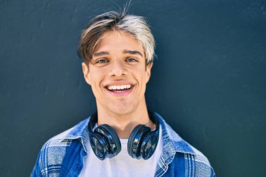 Şehirde kulaklık takarak mutlu gülümseyen genç İspanyol adam..