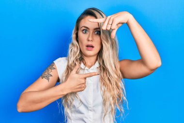 Güzel sarışın kadın resim çerçevesi hareketi yapıyor elleri şok olmuş, şüpheci ve alaycı görünüyor, ağzı açık kalınca şaşırıyor. 