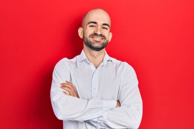 Zarif kıyafetler giyen genç kel adam kollarını kavuşturup kameraya bakarak gülümsüyor. pozitif kişi. 