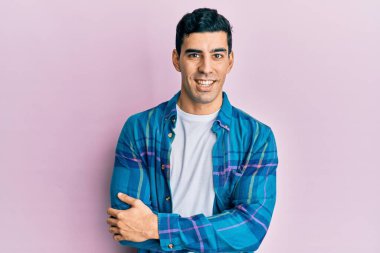 Yakışıklı, sıradan kıyafetler giyen mutlu yüzlü, kollarını kavuşturup kameraya bakan bir İspanyol. pozitif kişi. 