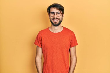 Yüzünde mutlu ve havalı bir gülümseme olan gündelik kıyafetler ve gözlük takan genç İspanyol bir adam. şanslı kişi. 