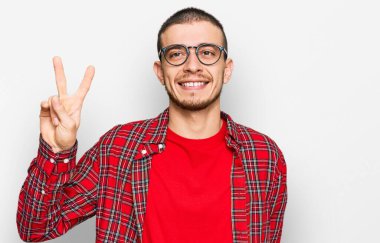 İspanyol genç adam gündelik giysiler giyip iki numarayı gösterip işaret ederken kendinden emin ve mutlu bir şekilde gülümsüyor.. 