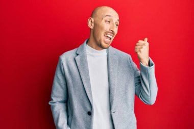 Sakallı, iş ceketli, baş parmağını kaldırmış, ağzı açık gülümseyen kel bir adam. 