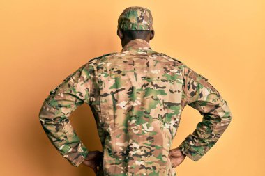 Askeri üniforma giyen genç Afro-Amerikan adam arkasını dönüp kollarını bedeninden ayırıyor. 