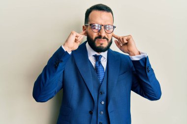 Sakallı, takım elbiseli, kravatlı, kulaklarını parmaklarıyla kapatan, gürültülü müzik sesi için rahatsız edici ifadeleri olan genç bir adam. sağır kavramı. 