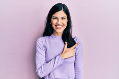 Gündelik kıyafetler giyen, neşeli, yüzünde bir gülümseme olan genç İspanyol kadın mutlu ve doğal bir ifadeyle elini ve parmağını kaldırdı. 