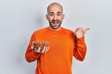 Fıstık tutan genç kel adam başparmağıyla yan tarafa bakıyor mutlu bir şekilde ağzı açık gülümsüyor. 