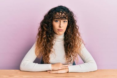 Gündelik giysiler giyen genç İspanyol kız depresif bir şekilde masada oturuyor ve üzüntüden ağlıyor, kızgın ve korkuyor. hüzünlü ifade. 