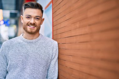 Genç beyaz adam gülümseyerek şehirde mutlu mesut duruyor..