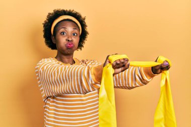 Spor giyim ve bileklik takan Afro-Amerikalı genç bir kadın komik yüzüyle yanaklarını şişiriyor. Ağzı havayla şişer, havayı yakalar.. 