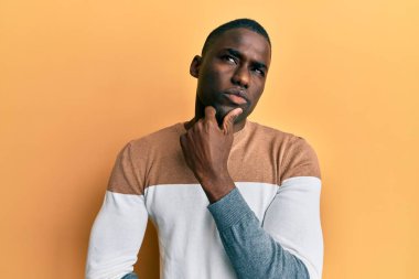 Elleri çenesinde gündelik giysiler giyen genç Afro-Amerikan bir adam soru soruyor, düşünceli bir ifade. Düşünceli bir yüzle gülümsüyor. şüphe kavramı. 