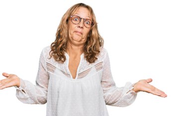 Orta yaşlı, beyaz gömlekli, gözlüklü, kafası karışık, elleri ve kolları havada sarışın bir kadın. şüphe kavramı. 