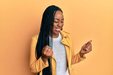 Başarı için heyecanlı, kolları havada ve gözleri kapalı, zaferi kutlamak için gülümseyen sıradan bir ceket giyen genç Afrikalı Amerikalı kadın. Kazanan konsept. 