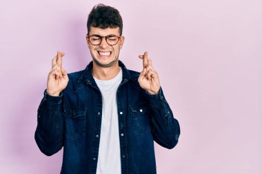 Gündelik kıyafetler giyen ve gözlüklü genç İspanyol adam umut ve gözlerin kapalı gülümseyerek el sallıyor. Şans ve batıl inançlar. 