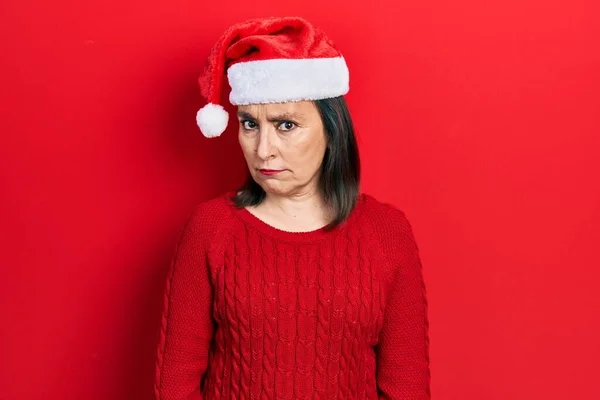 中世のヒスパニック系の女性のクリスマスの帽子懐疑的かつ神経を着て 問題のために動揺を眉をひそめている 否定的な人 — ストック写真