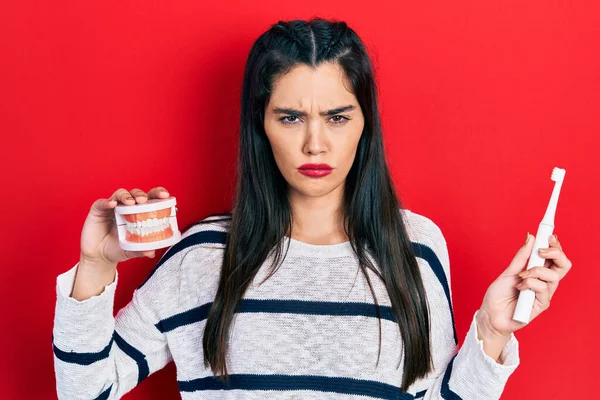 Chica Hispana Joven Sosteniendo Cepillo Dientes Eléctrico Dentadura Postiza Escéptico — Foto de Stock
