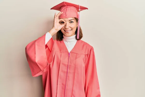 若いです白人女性を身に着けています卒業キャップと式のローブを身に着けています手笑顔でOkジェスチャーを行います 幸せな顔で指を通して見て — ストック写真