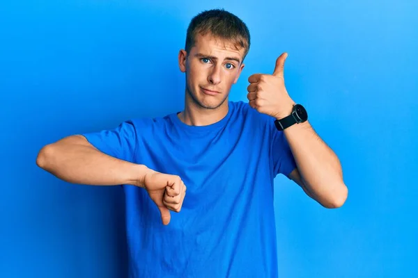 カジュアルなブルーのTシャツを着た若い白人男性が親指を上下に 意見の相違や合意表現をしています 狂気の葛藤 — ストック写真
