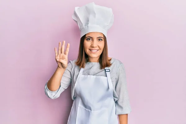 年轻而漂亮的女人穿着职业厨师的制服 头戴帽子 手握四号指尖 面带微笑 自信而快乐 — 图库照片