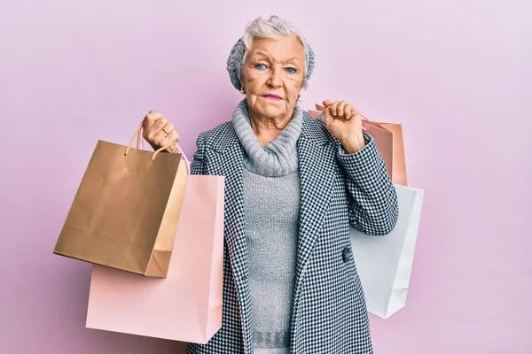 Senior Gråhårig Kvinna Som Håller Shoppingpåsar Avslappnade Med Allvarliga Ansiktsuttryck — Stockfoto