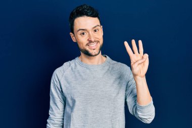 Gündelik kıyafetler giyen genç İspanyol adam üç numarayı gösterip işaret ederken kendinden emin ve mutlu gülümsüyor.. 