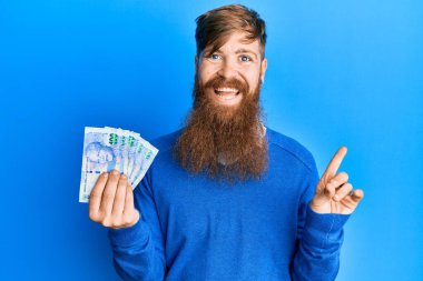 Genç İrlandalı kızıl saçlı adam Güney Afrika 'yı tutuyor. 100 rand' lık banknotlar gülümsüyor. 