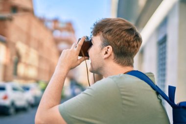 Beyaz tenli genç turist şehirde klasik kamera kullanarak mutlu bir şekilde gülümsüyor..