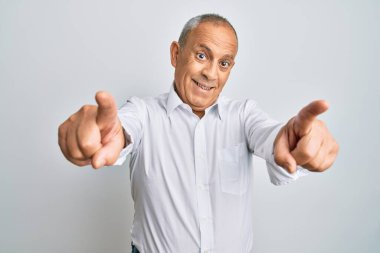 Yakışıklı, beyaz tişörtlü, seni ve kamerayı işaret eden, neşeli ve pozitif gülümseyen bir adam. 