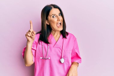 Doktor üniforması giyen orta yaşlı esmer kadın ve steteskop başarılı bir fikirle işaret ediyor. Heyecanlı ve mutlu. Bir numara.. 