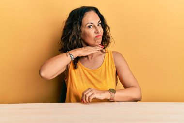 Güzel orta yaşlı kadın gündelik giysiler içinde masada oturmuş bıçak niyetine boğazını kesiyor, saldırganlığı şiddetle tehdit ediyor. 