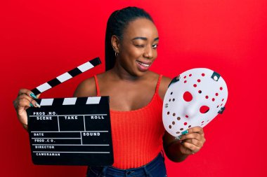 Genç Afro-Amerikan kadın elinde video film panosu ve korku maskesi ile kameraya seksi bir ifadeyle bakıyor, neşeli ve mutlu bir yüz.. 