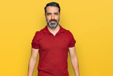 Orta yaşlı, sakallı, günlük kırmızı tişörtlü, pozitif ve mutlu görünen, kendine güvenen, gülümseyen, dişlerini gösteren bir adam. 