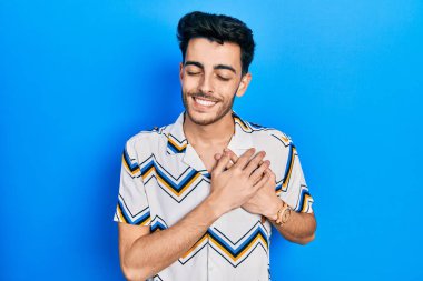 Gündelik kıyafetler giyen genç İspanyol adam elleri göğsünde, gözleri kapalı ve yüzünde minnet dolu bir jest ile gülümsüyor. sağlık kavramı. 