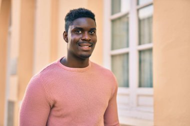 Genç Afrikalı Amerikalı adam gülümseyerek şehirde mutlu mesut duruyor..